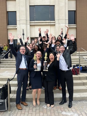 Group of young professionals celebrating with trophies outdoors.