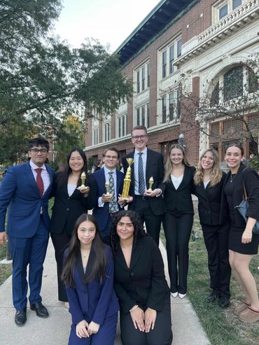 A group of young professionals posing outdoors with trophies in front of a brick building.