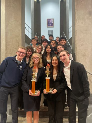 Group of young adults posing with trophies on stairs indoors.