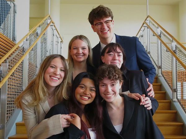 A group of six young adults smiling on a staircase.