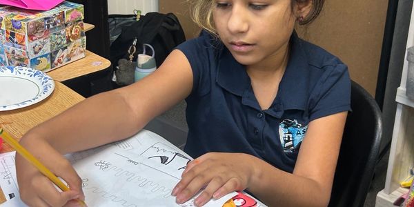 Young girl focused on writing in a workbook at a desk.