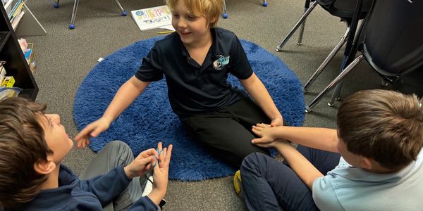 Three boys sitting on a classroom floor, interacting and smiling.