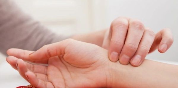 Person checking another's wrist pulse with fingers.