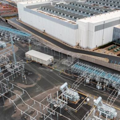 Aerial view of an electrical substation next to a large industrial building.