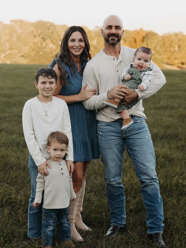 A happy family of five posing outdoors in a field during golden hour.