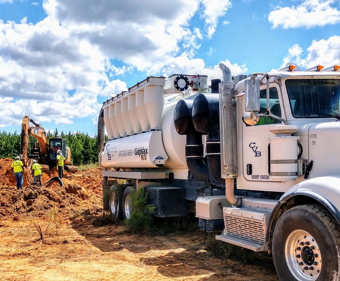 Large white industrial truck and workers at a construction site under a blue sky.
