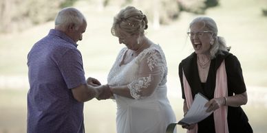 Celebrant Alison Moore laughing at Groom's comment as he places ring on bride's finger during weddin