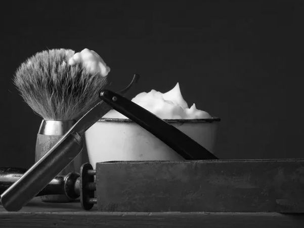 An artsy photo of a bowl of shaving cream, a straight razor and brush