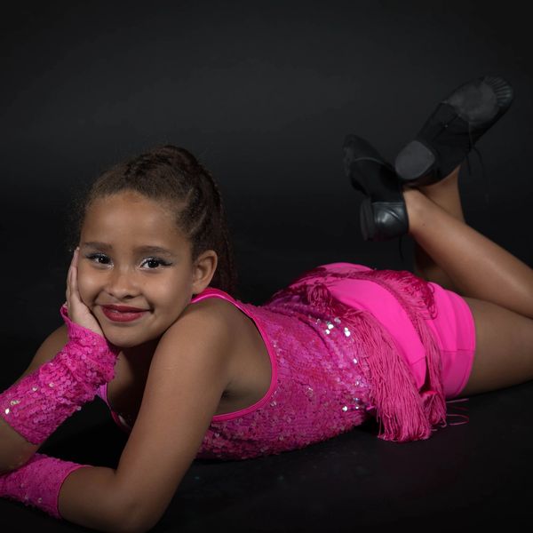 Girl posing in a pink sequined outfit against black background.