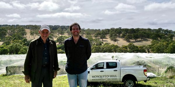 two men standing in front of a truck parked in a vineyard