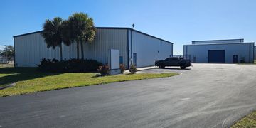 Industrial buildings with palm trees and parked car under clear blue sky.
