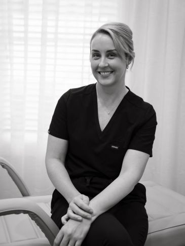 Registered Nurse Cassandra Baxter sitting in her clinic at Maison Avance Aesthetics in scrubs