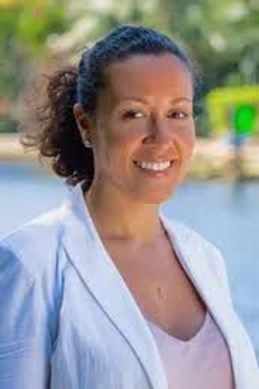 Smiling woman in white jacket outdoors by water.