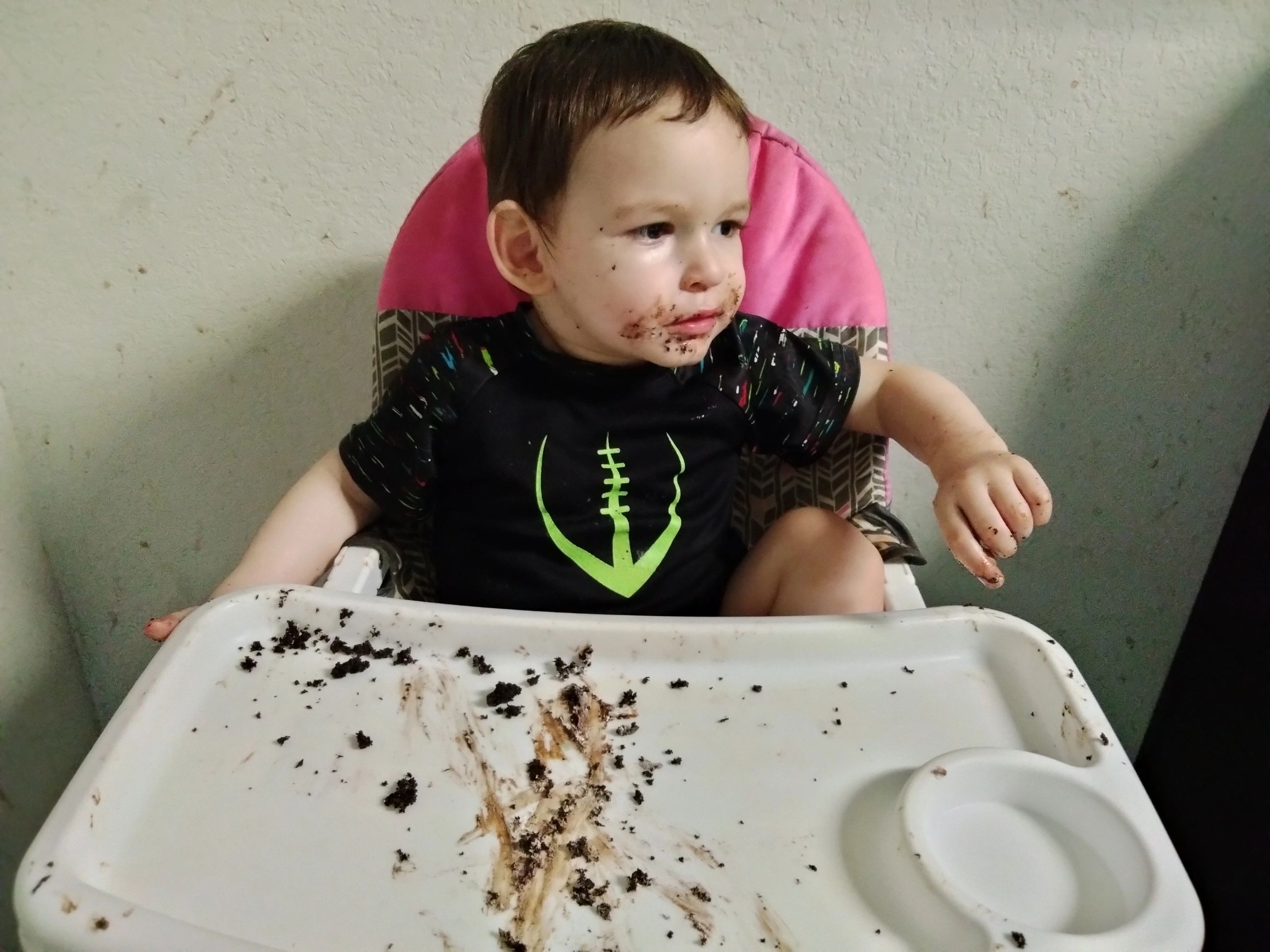 Toddler with a messy face and hands after eating in a high chair.