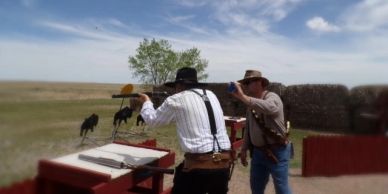 Two men dressed in cowboy attire aiming rifles at a shooting range outdoors.