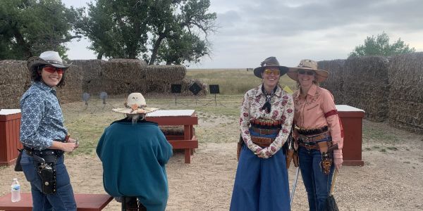 Four people dressed in cowboy attire at an outdoor shooting range.