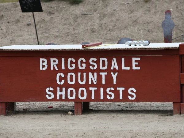 A sign reading 'Briggsdale County Shootists' on a wooden structure.