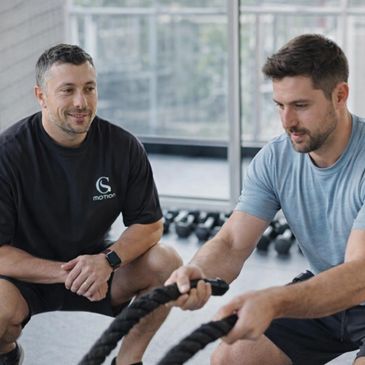 Personal trainer coaching a man using battle ropes in a gym.