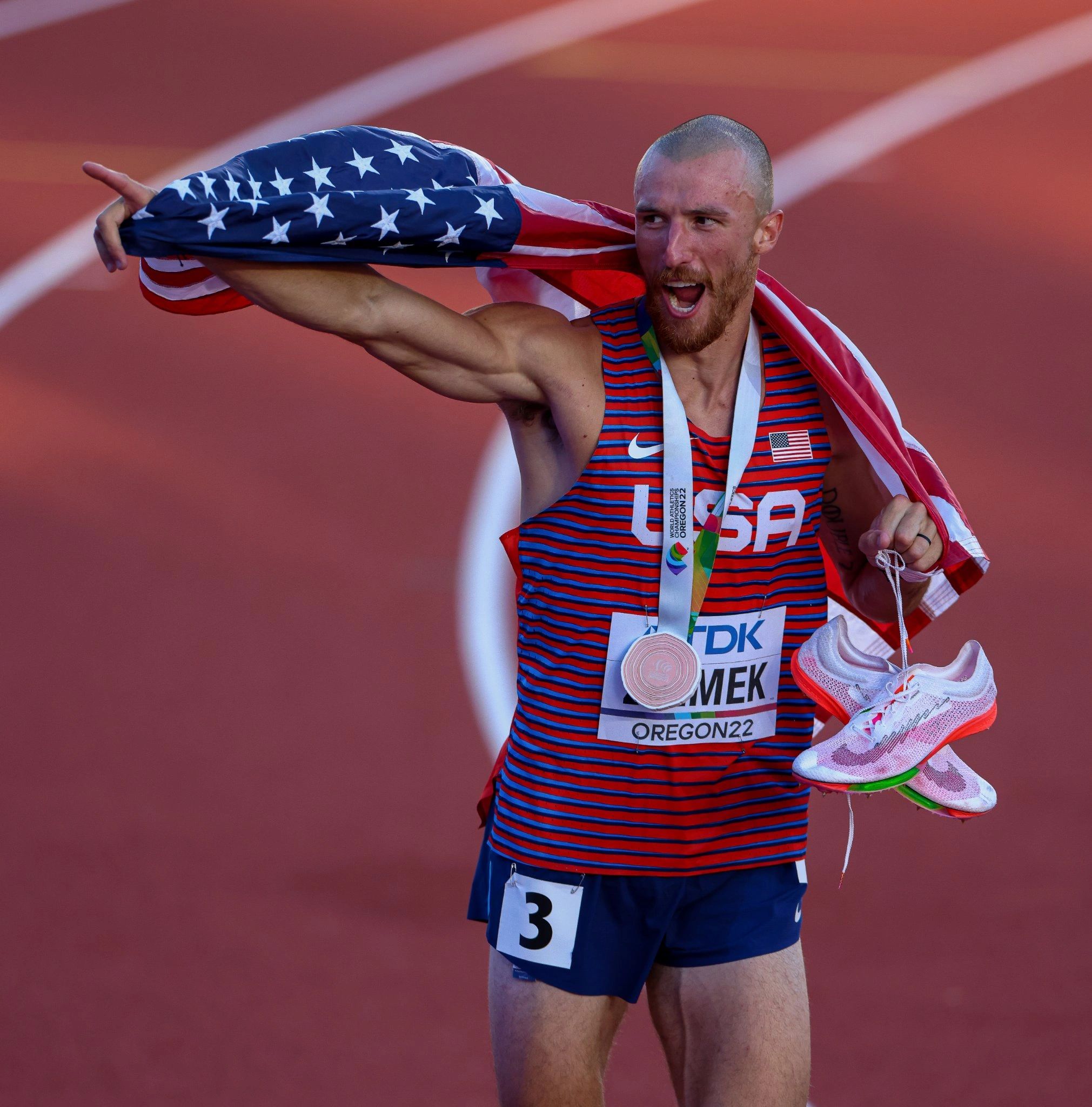American athlete celebrating victory with flag and medal on track.