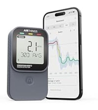 Portable air quality monitor displaying measurement next to smartphone showing data chart.