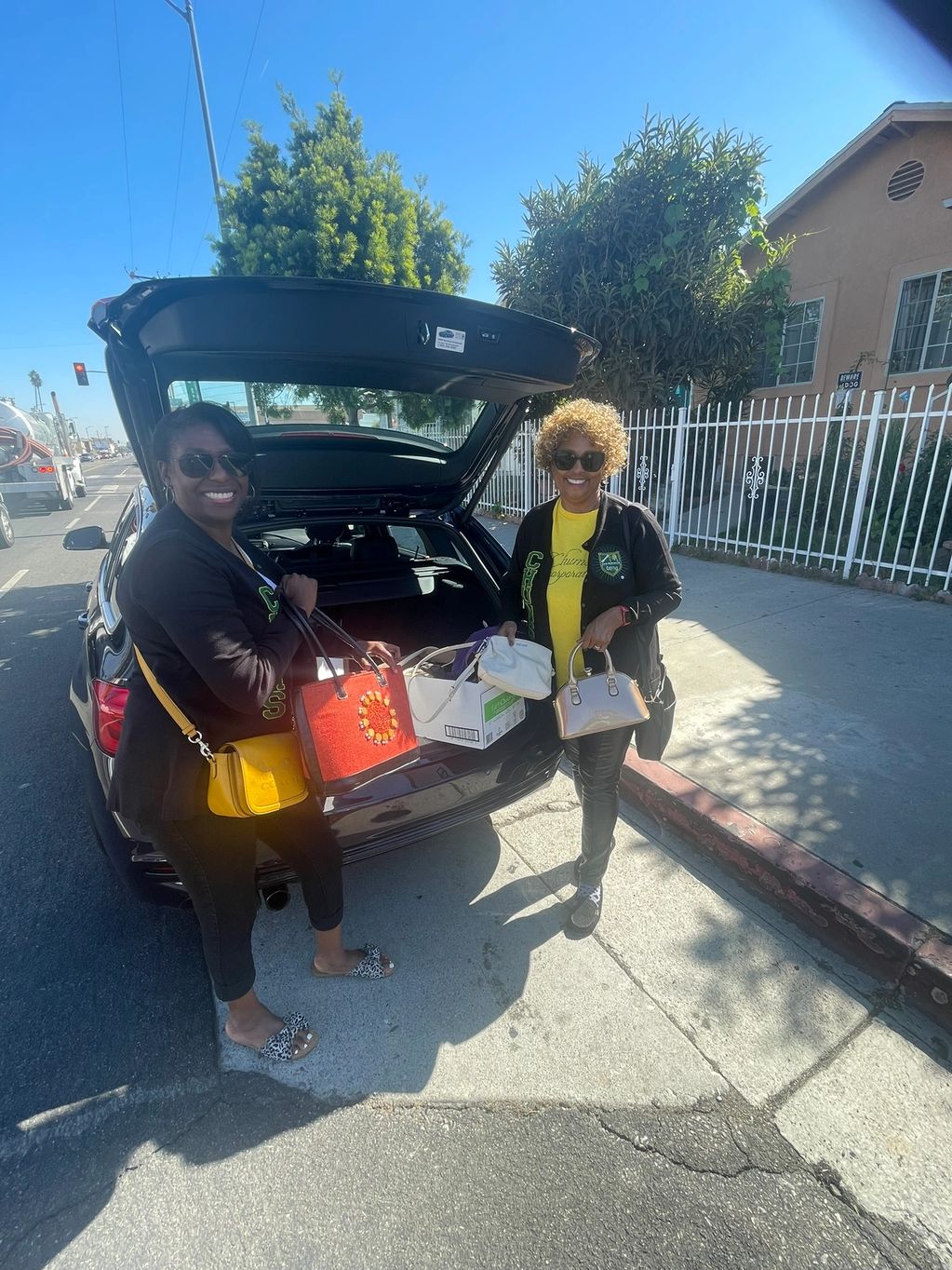 Two women smiling near an open car trunk on a sunny day.