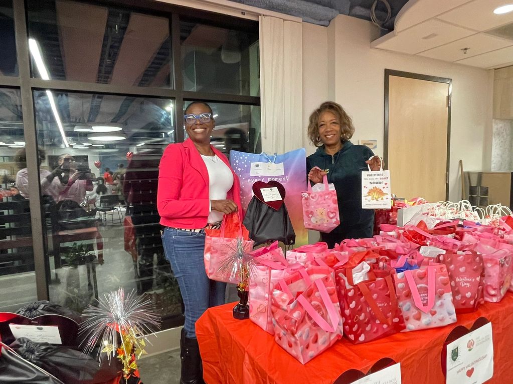 Two women with Valentine's Day gift bags smiling at a decorated table.