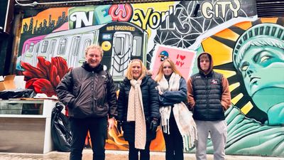 Four people posing in front of a vibrant New York City mural featuring a subway train and Statue of Liberty.