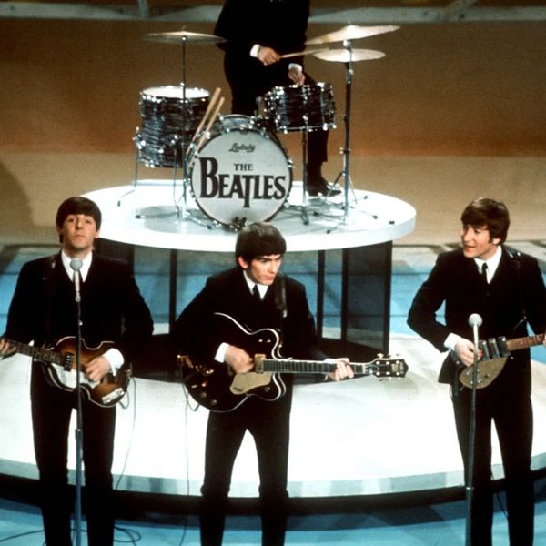 The Beatles performing on stage with instruments.