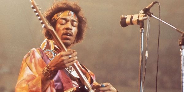 Jimi Hendrix playing guitar on stage with eyes closed.