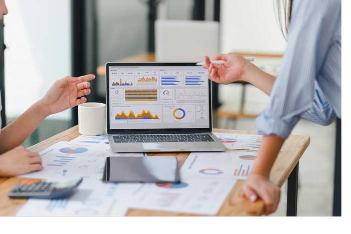Two people discussing sales data on a laptop with charts and graphs.