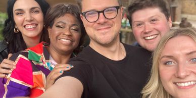 A group of five diverse friends smiling and taking a selfie outdoors.