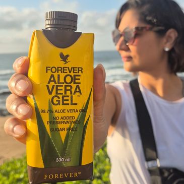 Person holding a yellow aloe vera gel carton on a beach.