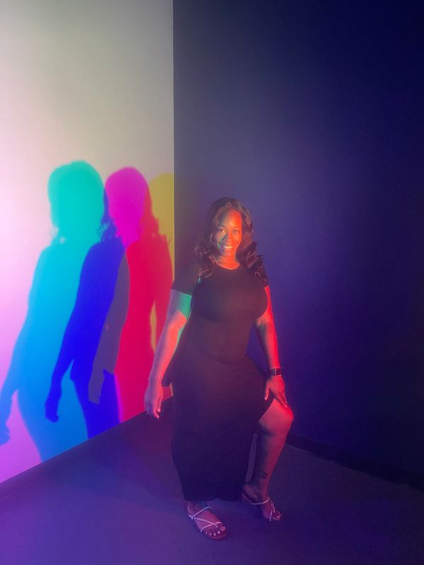 Woman in black dress with colorful shadows on the wall.