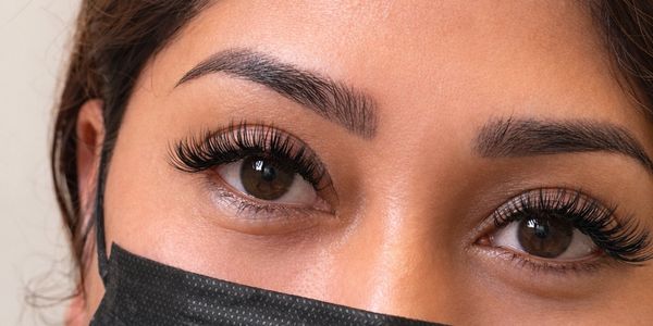 Close-up of a woman with long eyelashes wearing a black face mask.