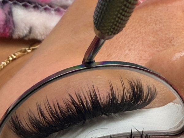 Close-up of eyelash extension application with a tool and glasses.