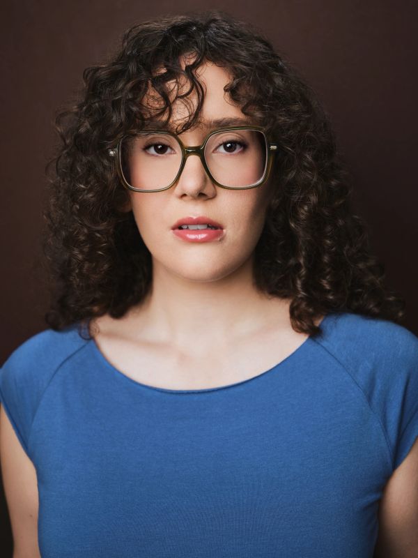 Woman with curly hair and glasses wearing a blue top.