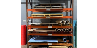 Shelves with various tubes, sheets, and materials in a storage area.