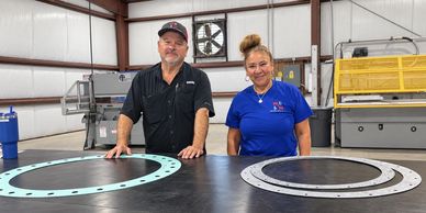 Two people standing behind metal ring parts on a table.