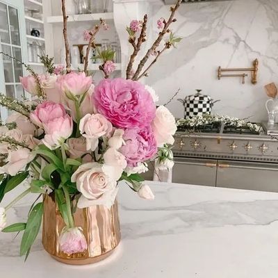 Elegant bouquet of pink and white flowers in a gold vase on a marble kitchen counter.