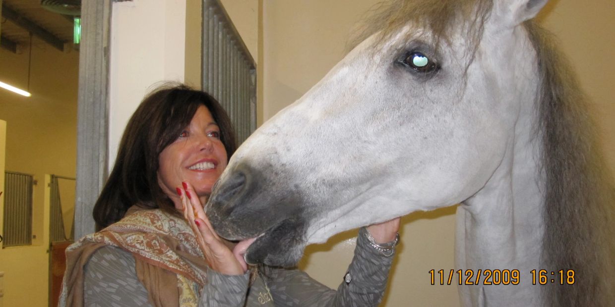 Woman smiling and petting a white horse indoors.
