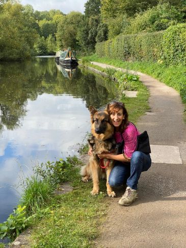 Woman hugging a German Shepherd by a riverside path.