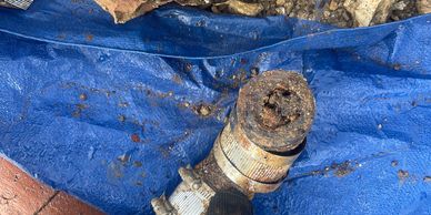 Rusty, corroded pipe and broken terracotta pipe on a blue tarp with dirt and rocks.