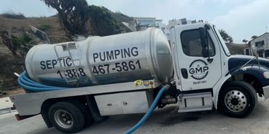 Septic pumping truck with blue hoses connected to manholes on pavement.
