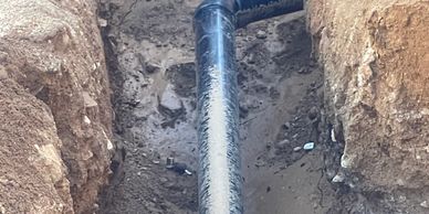 Black pipeline installed in a dirt trench with an elbow joint.