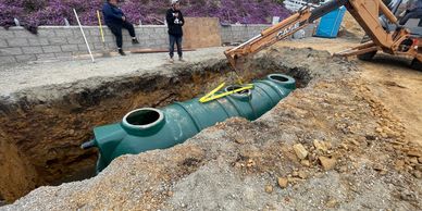 Workers install a large green septic tank in a construction site trench.