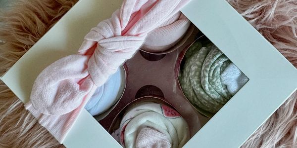 Gift box with baby socks and a pink bow, on a soft pink fur background.