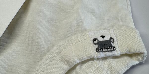 Close-up of a white fabric tag with a quirky face design on a white garment.