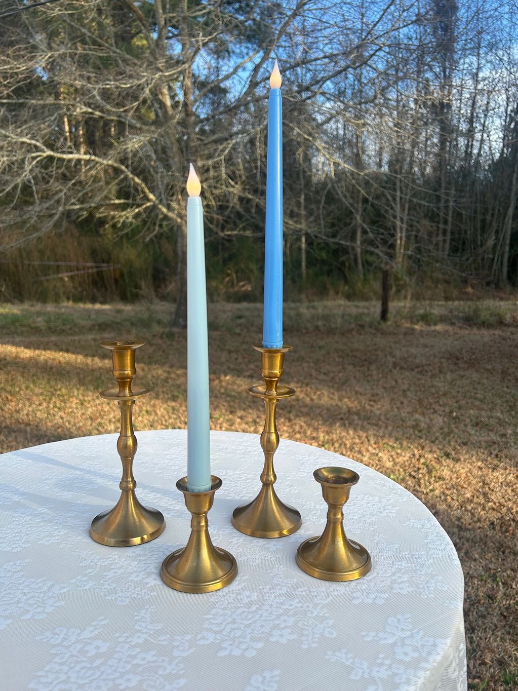 Gold candlestick holders with blue candlesticks in front of woodsy background