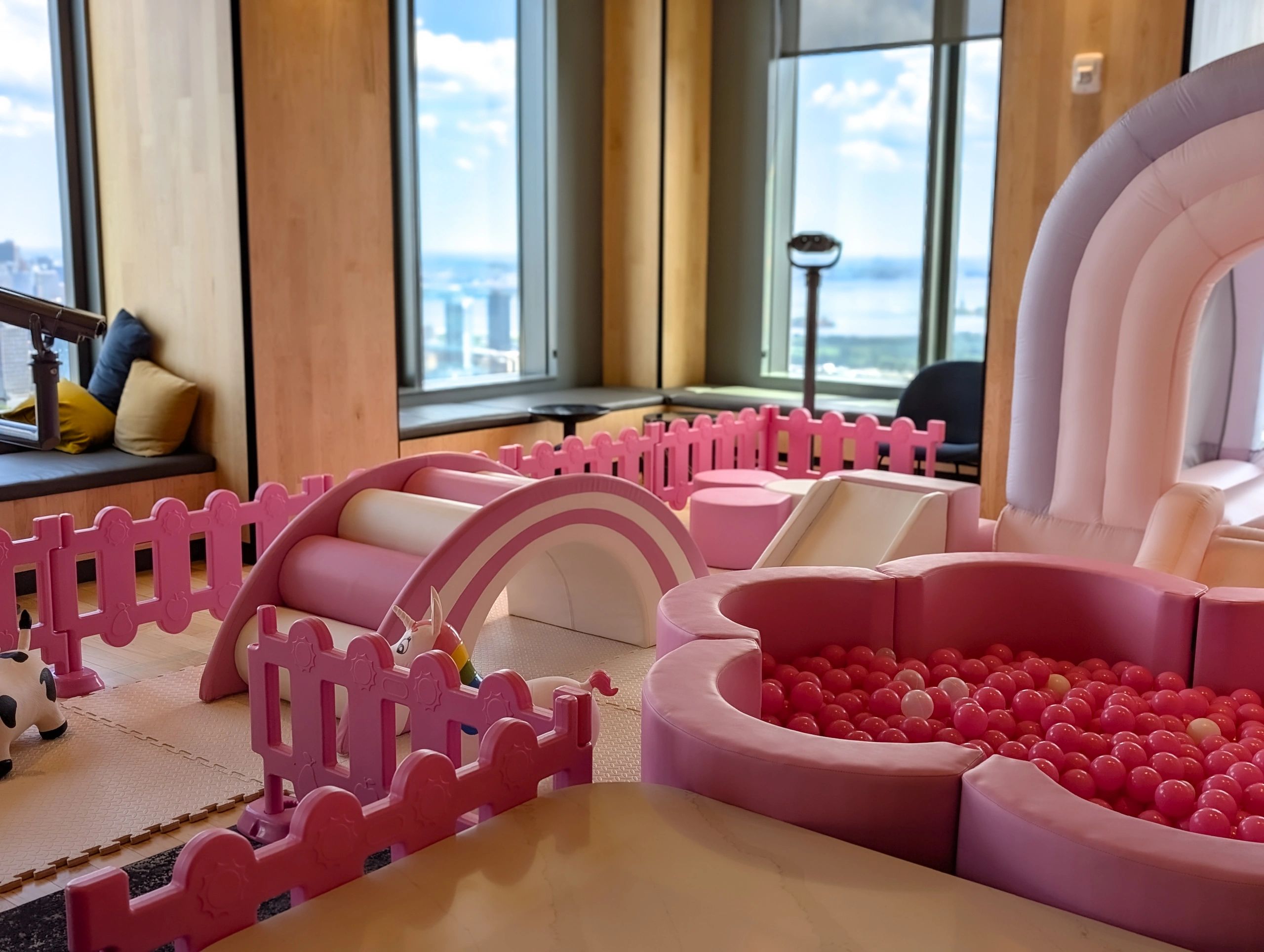 A pink-themed indoor play area with a ball pit and slide near large windows.