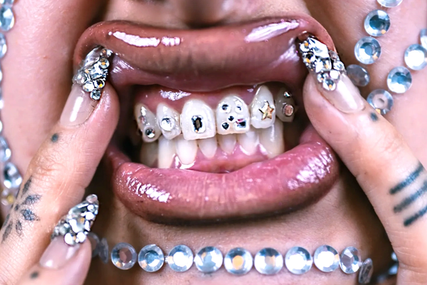 Person with jeweled nails, facial gems, and tooth gems